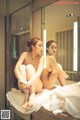 A naked woman sitting on a towel in front of a mirror.