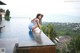 A woman in a blue dress and straw hat sitting on the edge of a swimming pool.