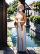 A woman in a long white dress standing next to a pond.