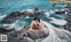 a bride and groom sitting on a rock by the ocean