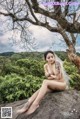 A woman sitting on top of a rock next to a tree.