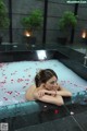 A woman laying in a bathtub with rose petals on the floor.