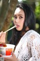 A woman holding a bowl of food with chopsticks in her mouth.