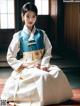 A woman in a blue and white hanbok sitting on the floor.