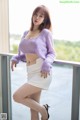 A woman in a purple sweater and white skirt posing on a balcony.