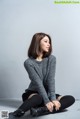 A woman sitting on the ground wearing a gray sweater and black skirt.