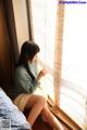 A woman sitting on a bed looking out a window.