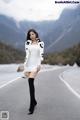 A woman in a white dress and black boots standing on a road.