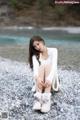 A woman sitting on a rocky beach next to a river.