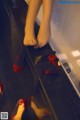 A woman's feet in a mirror with red shoes on the floor.