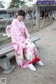 A woman in a pink kimono sitting on a bench.