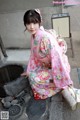 A woman in a pink kimono sitting on the ground.