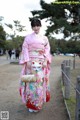 A woman in a pink kimono is walking down a dirt road.