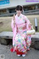 A woman in a pink kimono sitting on a bench.