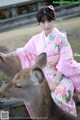 A woman in a pink kimono sitting next to a deer.