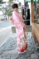 A woman in a pink kimono standing on a cobblestone street.