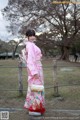 A woman in a pink kimono standing next to a fence.