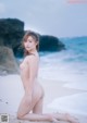 A naked woman sitting on a beach next to the ocean.