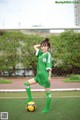 A woman in a green soccer uniform posing with a soccer ball.