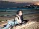 A woman laying on the ground next to the ocean.