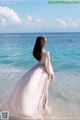 A woman in a long dress standing in the ocean.