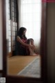 A woman sitting on the floor in front of a window.