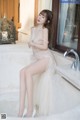 A woman in a white dress sitting on a bathtub.