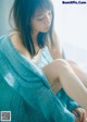 A woman sitting on a window sill wearing a blue sweater.