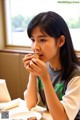 A young girl sitting at a table eating a piece of food.