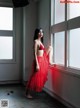 A woman in a red dress leaning against a window.