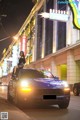 A woman sitting on top of a car in the middle of a city.