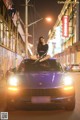 A woman sitting on top of a blue car in the middle of a street.